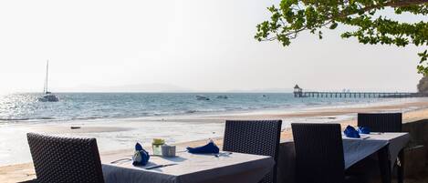 A seaside restaurant with tables set for dining, overlooking the ocean and a pier.