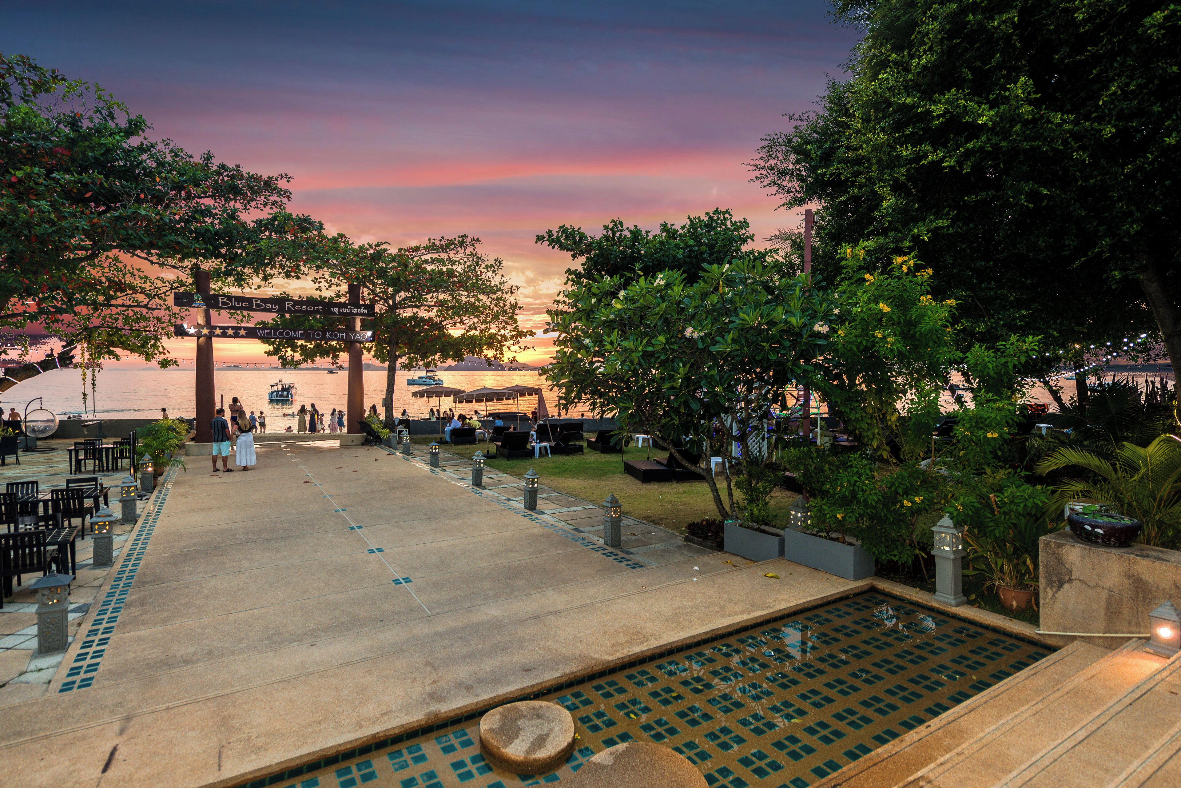A resort pool area with a sunset view, outdoor seating, and a sign welcoming guests.