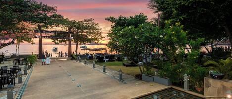 A resort pool area with a sunset view, outdoor seating, and a sign welcoming guests.