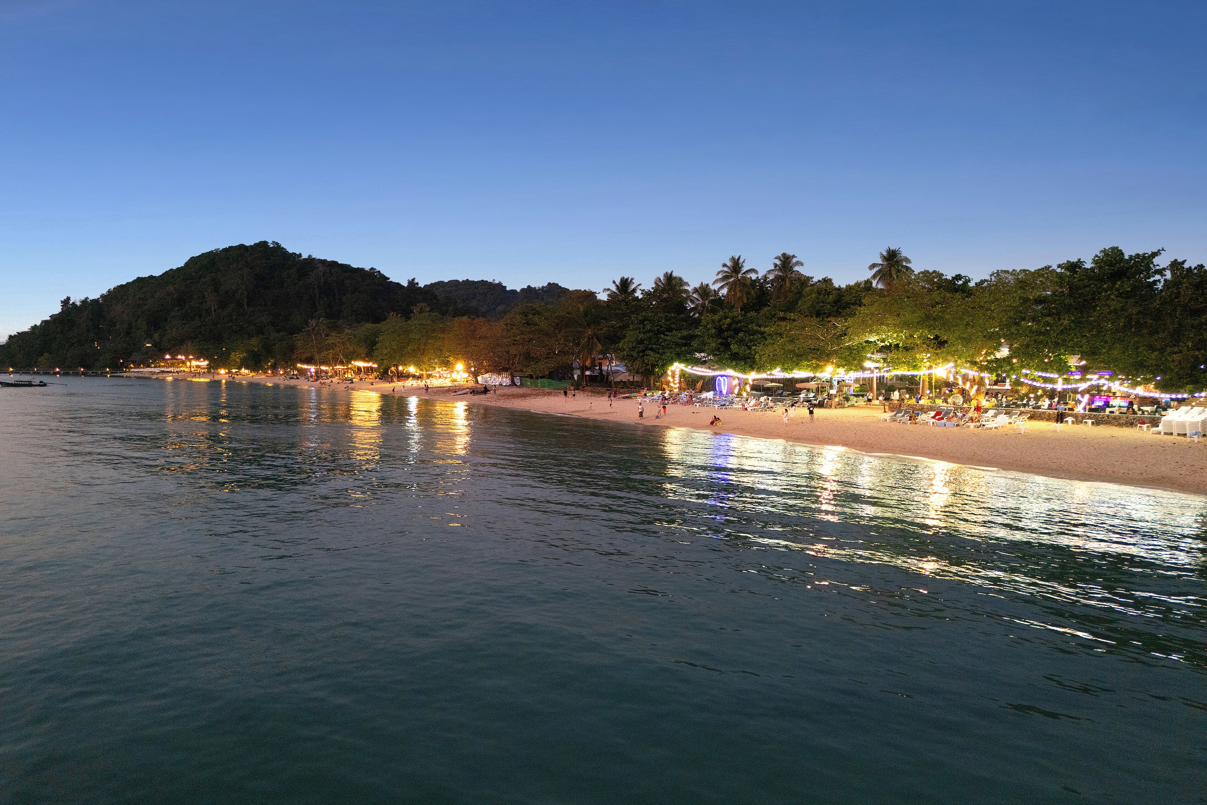 A beach with a calm sea, palm trees, and a hill in the background.