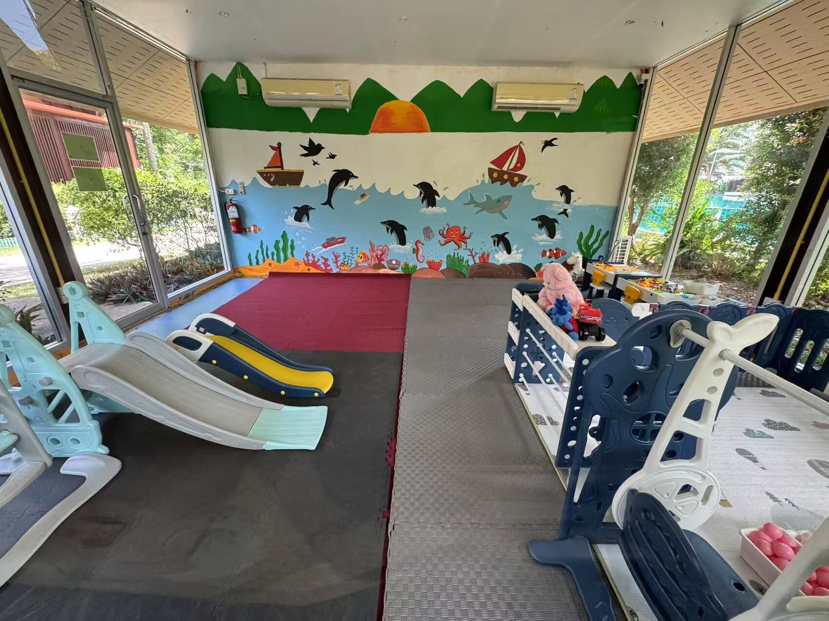 Zona de juegos infantiles con toboganes y un mural de vida marina.