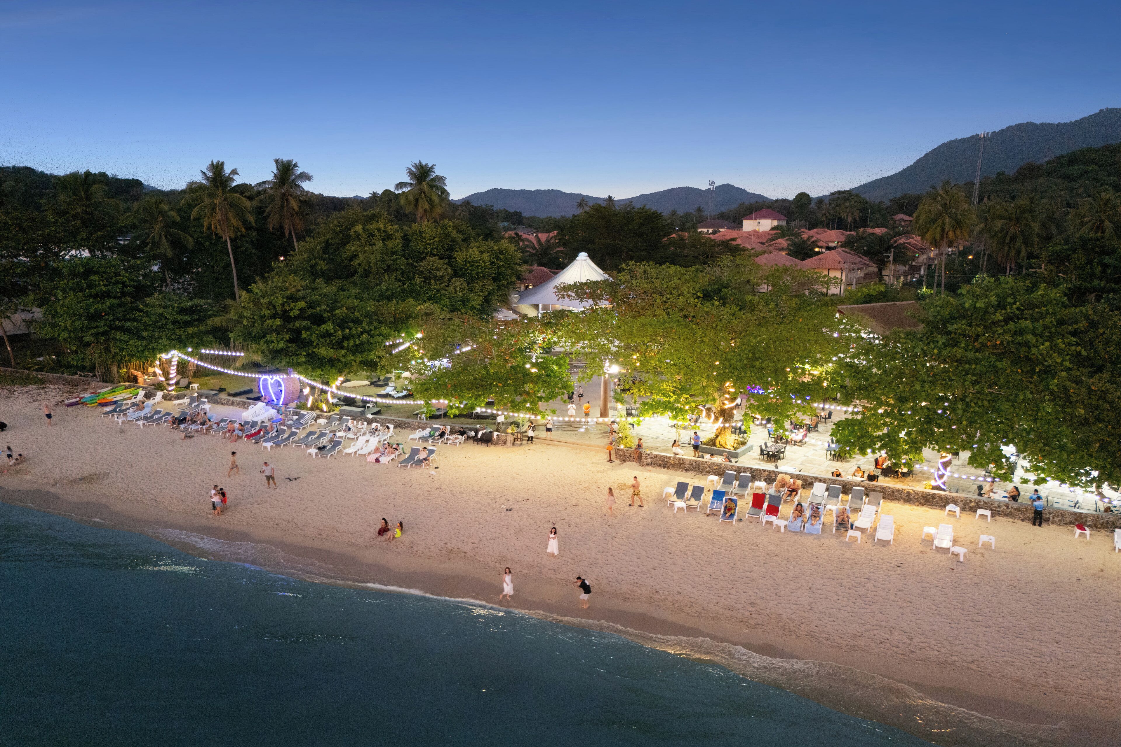 A beach with a white tent, palm trees, and a mountain in the background.