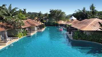A swimming pool with a clear blue water, surrounded by palm trees and buildings with tiled roofs.