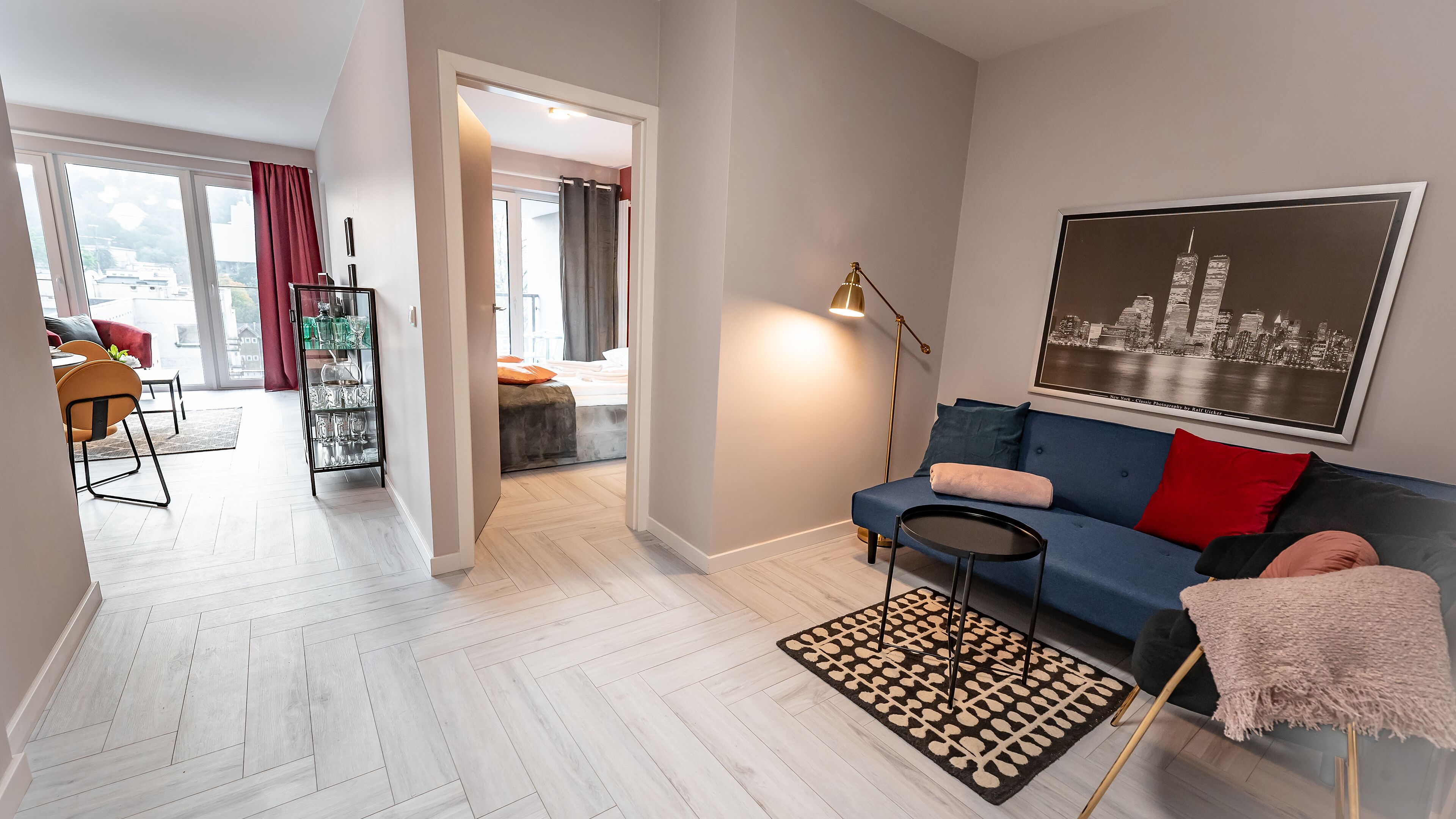 A modern living room with a blue sofa, a small round table, and a patterned rug. A glass cabinet with decorative items is visible in the background.