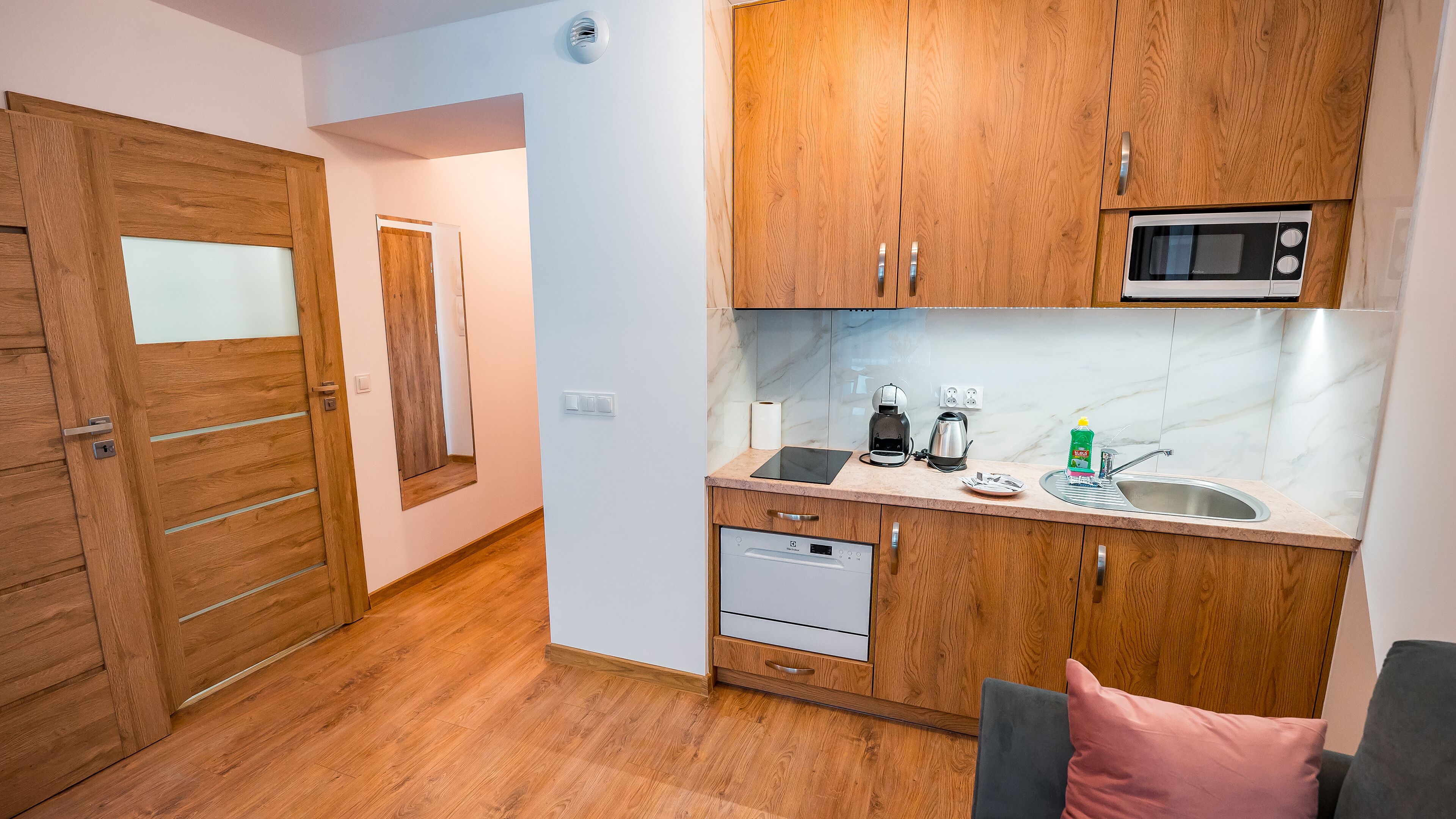 Eine kompakte Küche mit Holzschränken, einer Mikrowelle, einer Kaffeemaschine und einem Geschirrspüler.