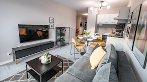A modern living room with a flat-screen TV, sofa, coffee table, and dining area with chairs. - Apartamenty Sun & Snow Cicha (Krynica-Zdroj)