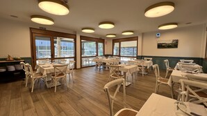 Comedor con varias mesas y sillas, ventanas amplias e iluminación en el techo.
