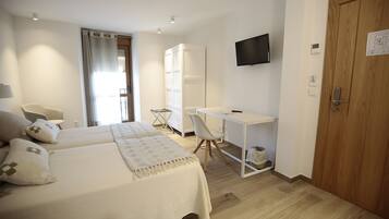 A bedroom with two beds, a desk, a chair, a TV, and a wardrobe.