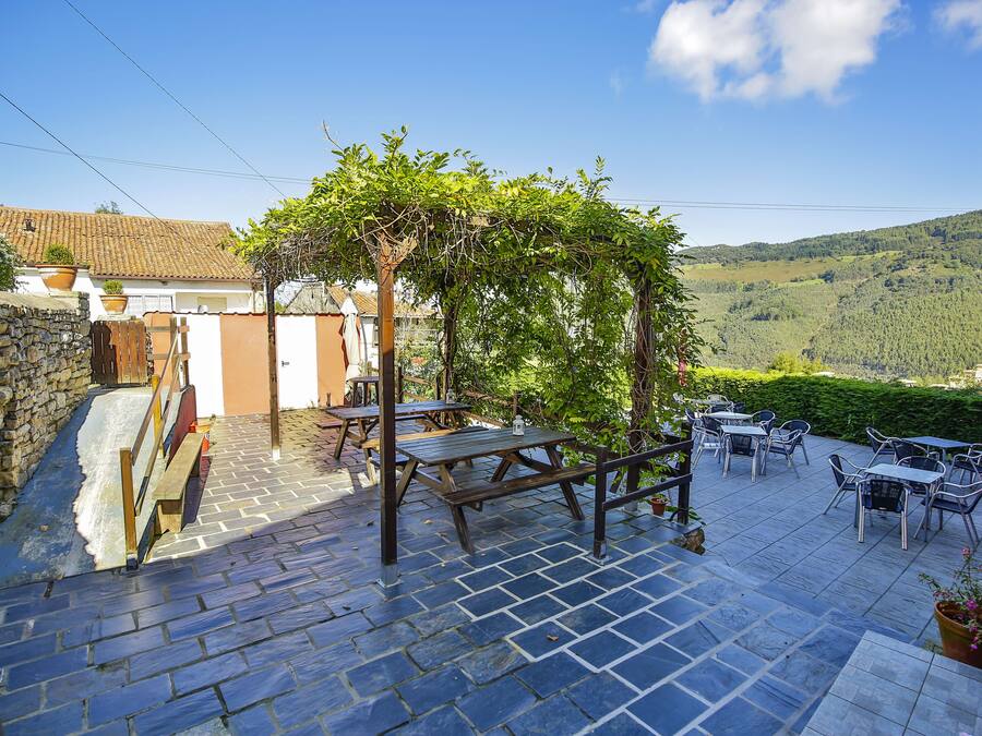 A patio with stone flooring, wooden tables, and a pergola covered in greenery.