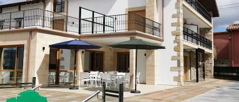 A two-story building with a balcony, outdoor seating area, and a stone facade.