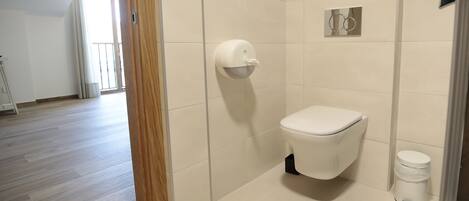 Un baño moderno con inodoro, secamanos y cubo de basura.