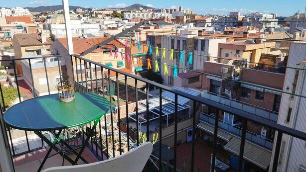 A balcony with a green table and a white chair, overlooking a residential area with colorful laundry hanging. - Feel Welcome Barcelona Splau (Cornella de Llobregat)