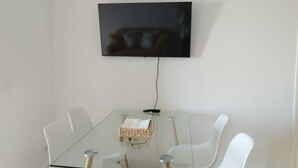 A modern dining area with a glass table, white chairs, and a mounted flat-screen TV. - Feel Welcome Barcelona Splau (Cornella de Llobregat)