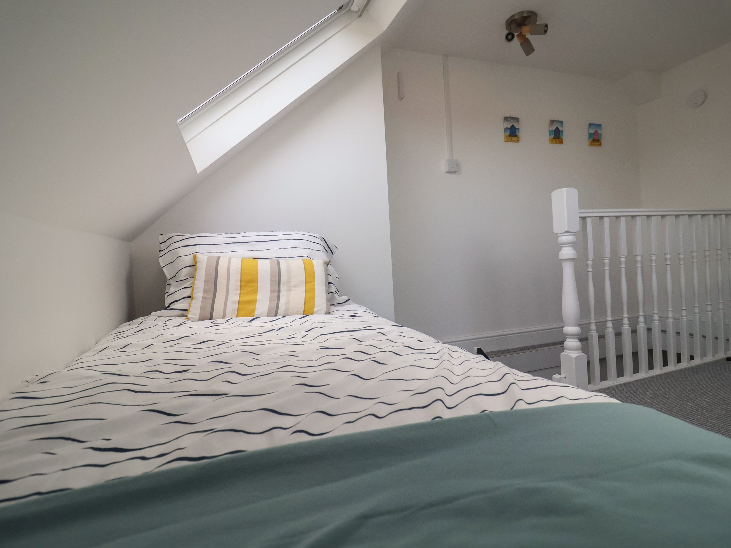 Ein Schlafzimmer mit schrägverdeckter Decke, einem Bett mit gestreifter Bettwäsche, einem weißen Babybett und einem kleinen Fenster.