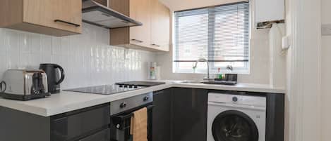 A compact kitchen with a built-in oven, a washing machine, and a window with blinds.