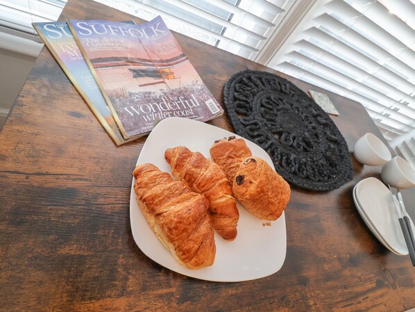 Una mesa de madera con una revista, un plato de croissants y un posavasos de punto negro.