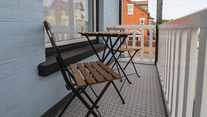 Un balcone con panchina e tavolino in legno, ringhiera bianca e vista sulle case vicine.