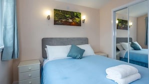 A bedroom with a bed, a nightstand, a wall-mounted painting, and a mirror. - Kilninver Chalet on Reelig Estate (Inverness)