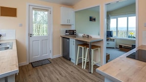 A compact kitchen with a microwave, a sink, and a door leading to a balcony. - Kilninver Chalet on Reelig Estate (Inverness)