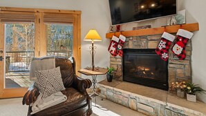 Una sala de estar acogedora con chimenea, un sofá de cuero, una mesa con lámpara y un televisor montado en la pared.