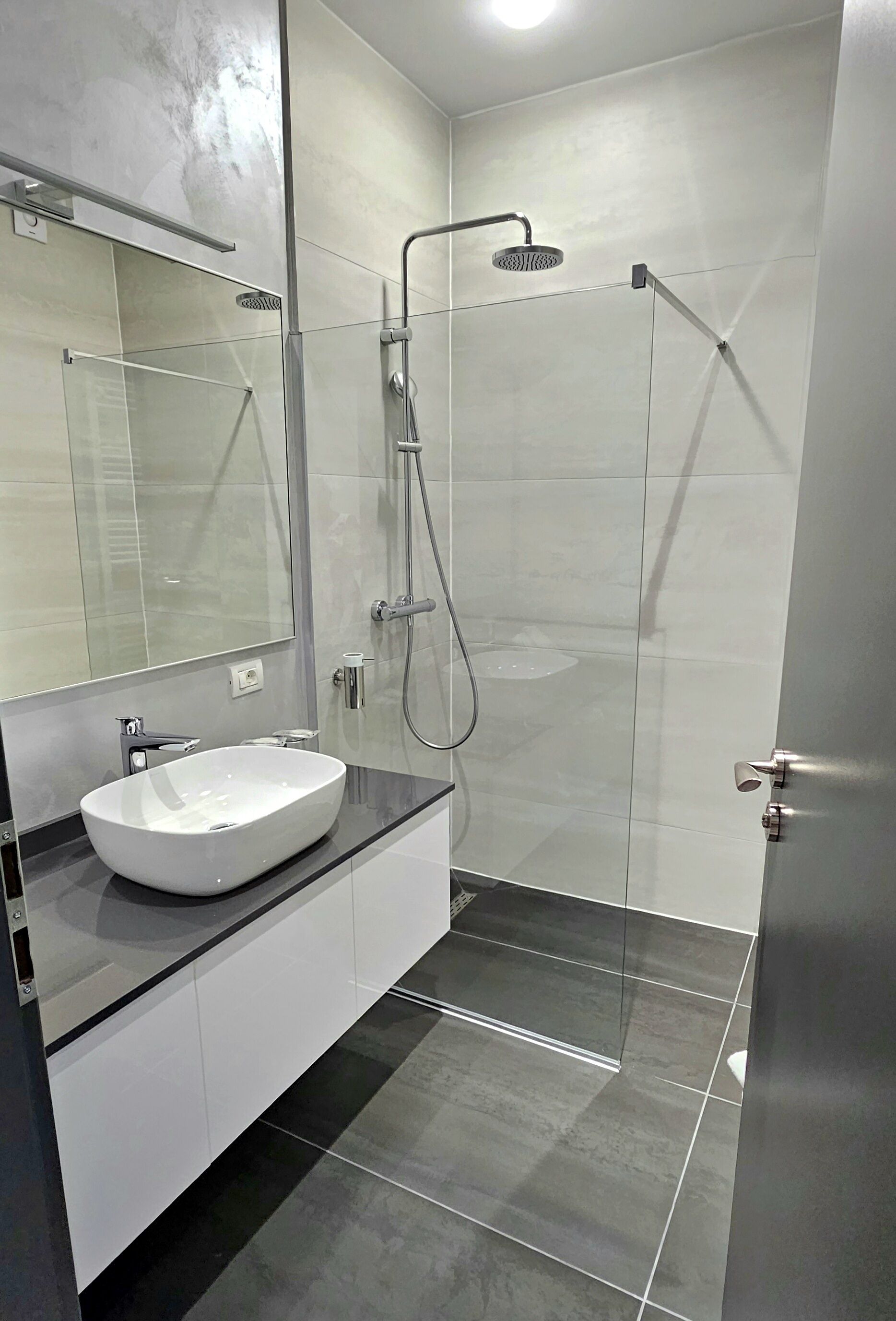 A modern bathroom with a glass-enclosed shower, a white sink, and a large mirror.