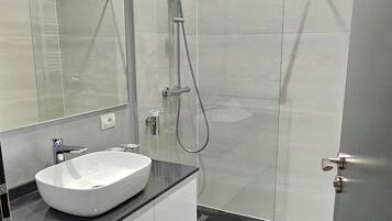 A modern bathroom with a glass-enclosed shower, a white sink, and a large mirror.