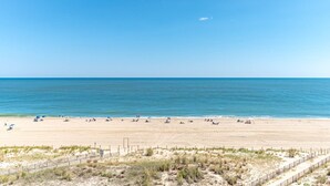 Een breed zandstrand met een helderblauwe lucht en een rustige zee.
