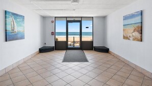Eine Hotelhalle mit Blick auf den Strand, einem Fliesenboden und Kunstwerken an den Wänden.