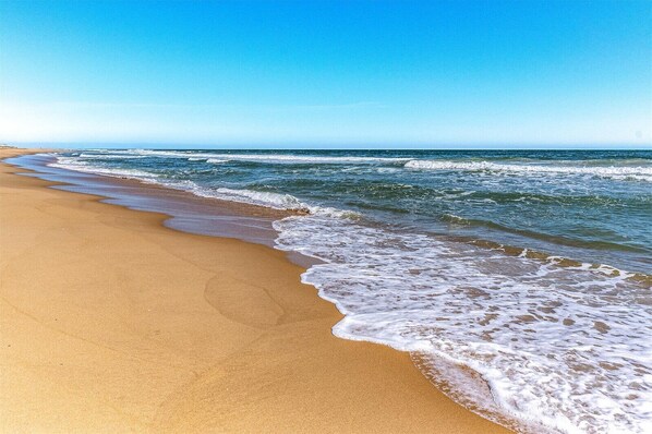 Una playa con orilla arenosa y olas lamiendo suavemente la costa.