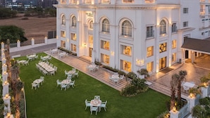 Un hotel con un amplio espacio exterior que cuenta con varias mesas y sillas de comedor, un césped bien cuidado y un edificio de varios pisos con balcones.