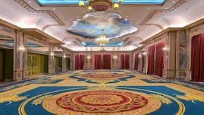 Un salón imponente con una alfombra grande y elaborada, un candelabro y cortinas rojas.