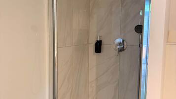 A modern shower enclosure with a glass door, a handheld showerhead, and a wall-mounted faucet.
