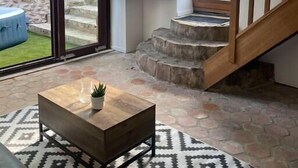 Un salon moderne avec un sol en pierre, une table basse en bois, un tapis à motifs, un escalier et un téléviseur fixé au mur.