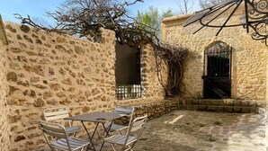Un espace extérieur entouré de murs en pierre, avec une table et des chaises, un portail en fer forgé et un chemin en pierre.