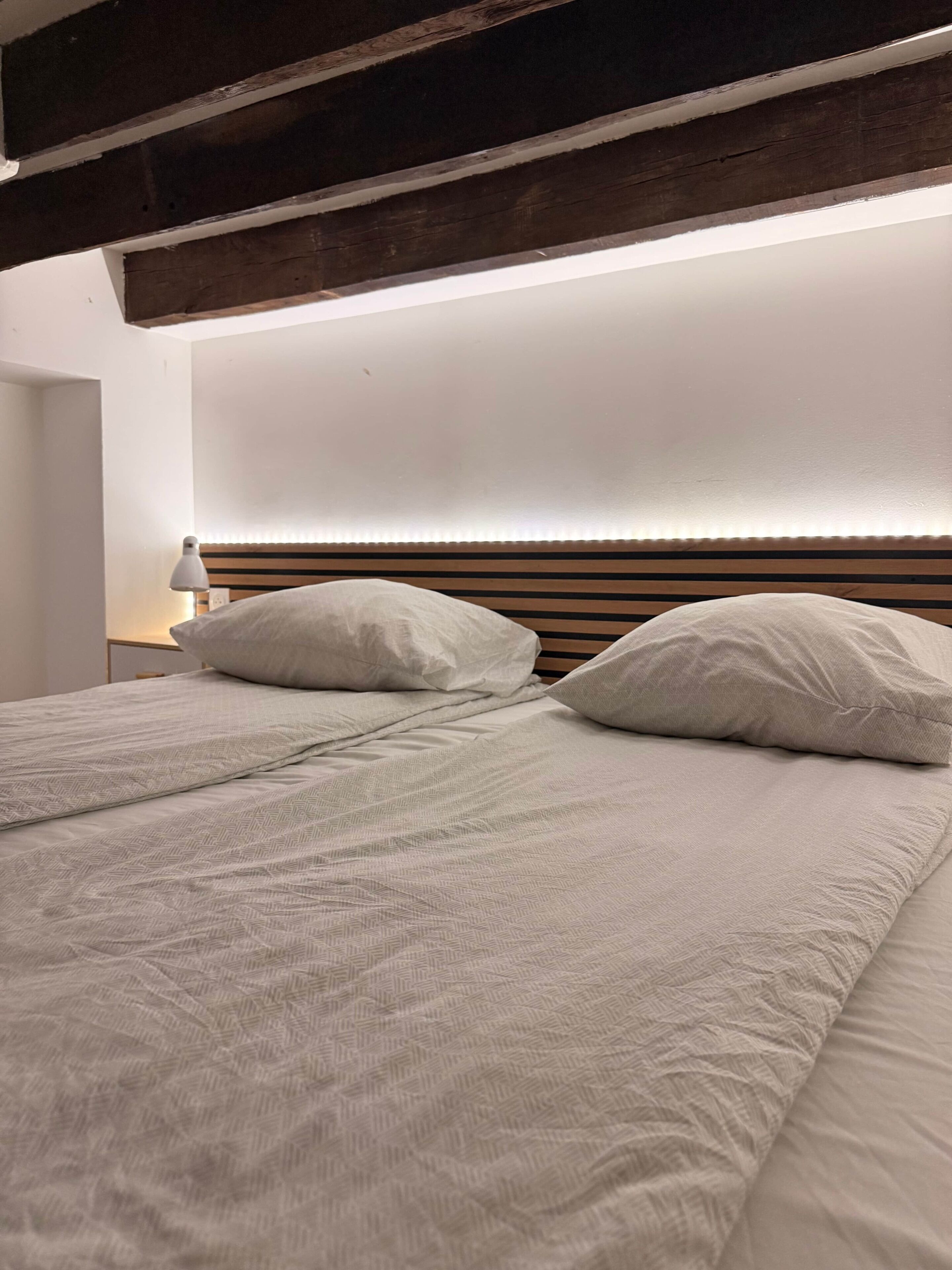 A bed with a wooden headboard, two pillows, and a bedside lamp.