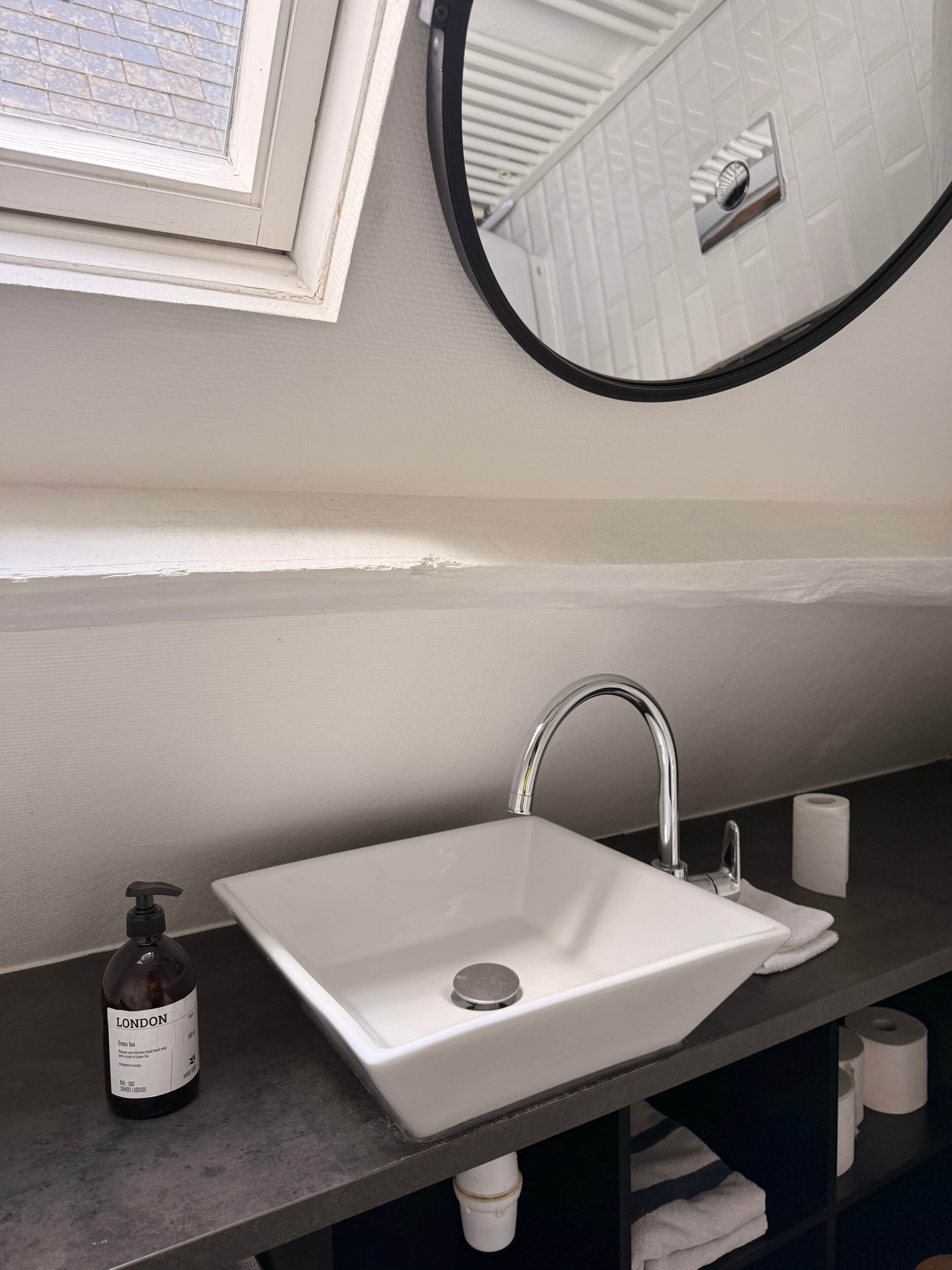 A bathroom with a white sink, a mirror, a bottle of green tea soap, and a toilet paper roll.
