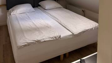 A single bed with a dark headboard, a white mattress, and a light-colored blanket. There is a window with a view of a building outside.