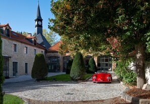 A cobblestone driveway leading to a building with a clock tower, surrounded by well-maintained hedges and trees.