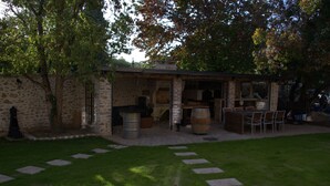 Un bâtiment en pierre avec une terrasse en briques, des sièges extérieurs et un tonneau.