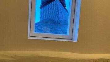 Une fenêtre donnant sur le coin d’un bâtiment, avec notamment une tour horloge.