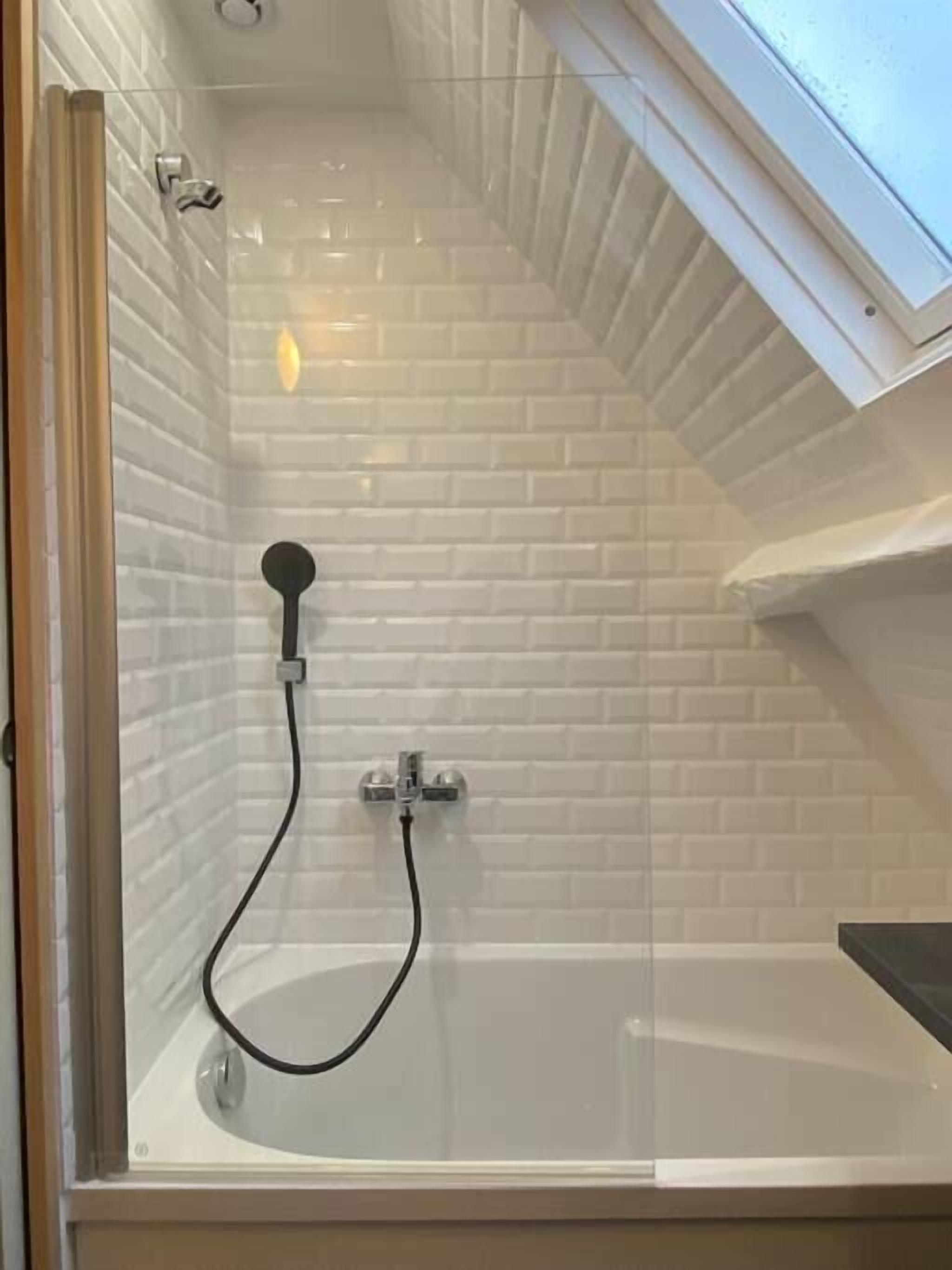 A modern shower with a glass enclosure, white tiled walls, and a skylight.