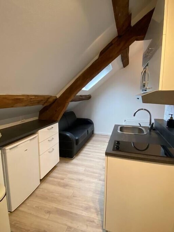 A compact kitchen with a built-in sink, white cabinets, and a black countertop. There is a black sofa and a skylight above the kitchen.