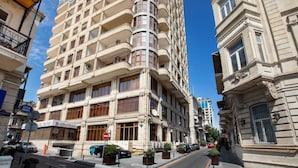Un hôtel à plusieurs étages doté de balcons, un ciel dégagé et une rue animée par des voitures et des piétons.
