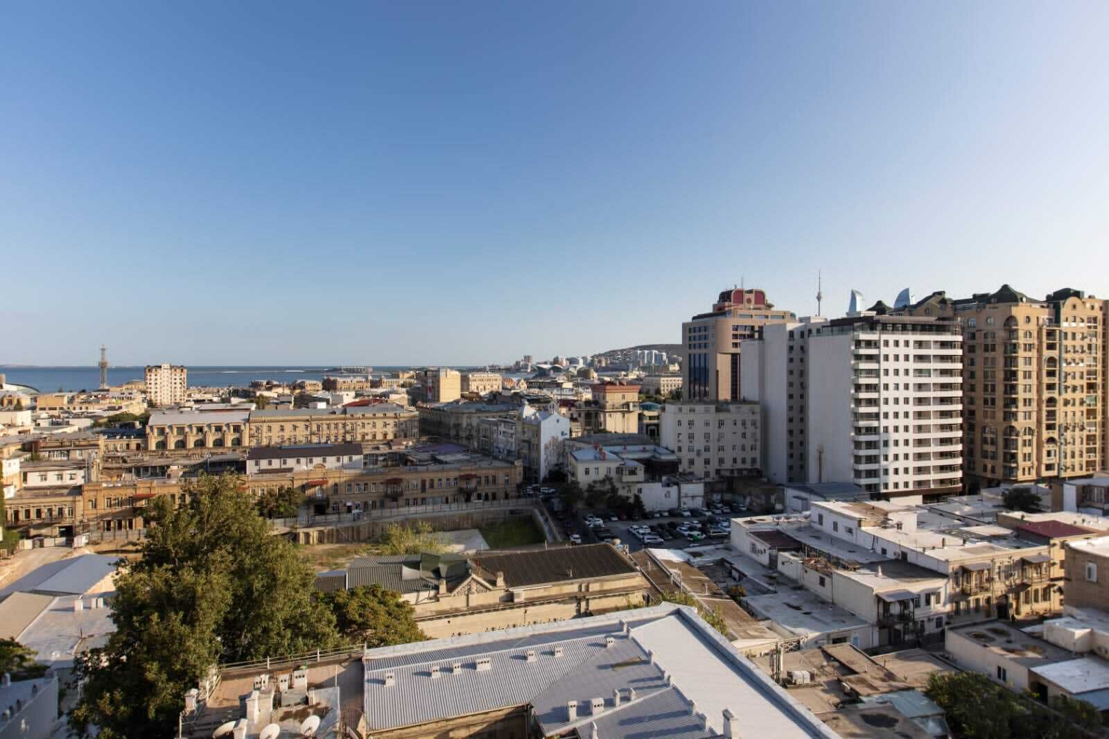 Un paisaje urbano con una mezcla de edificios históricos y modernos, cielo despejado y vista al mar en la distancia.