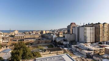 Un paisaje urbano con una mezcla de edificios históricos y modernos, cielo despejado y vista al mar en la distancia.
