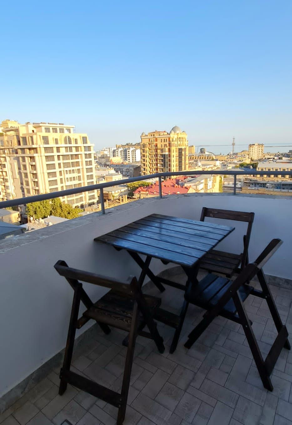 A balcony with a table and chairs, overlooking a cityscape with various buildings.