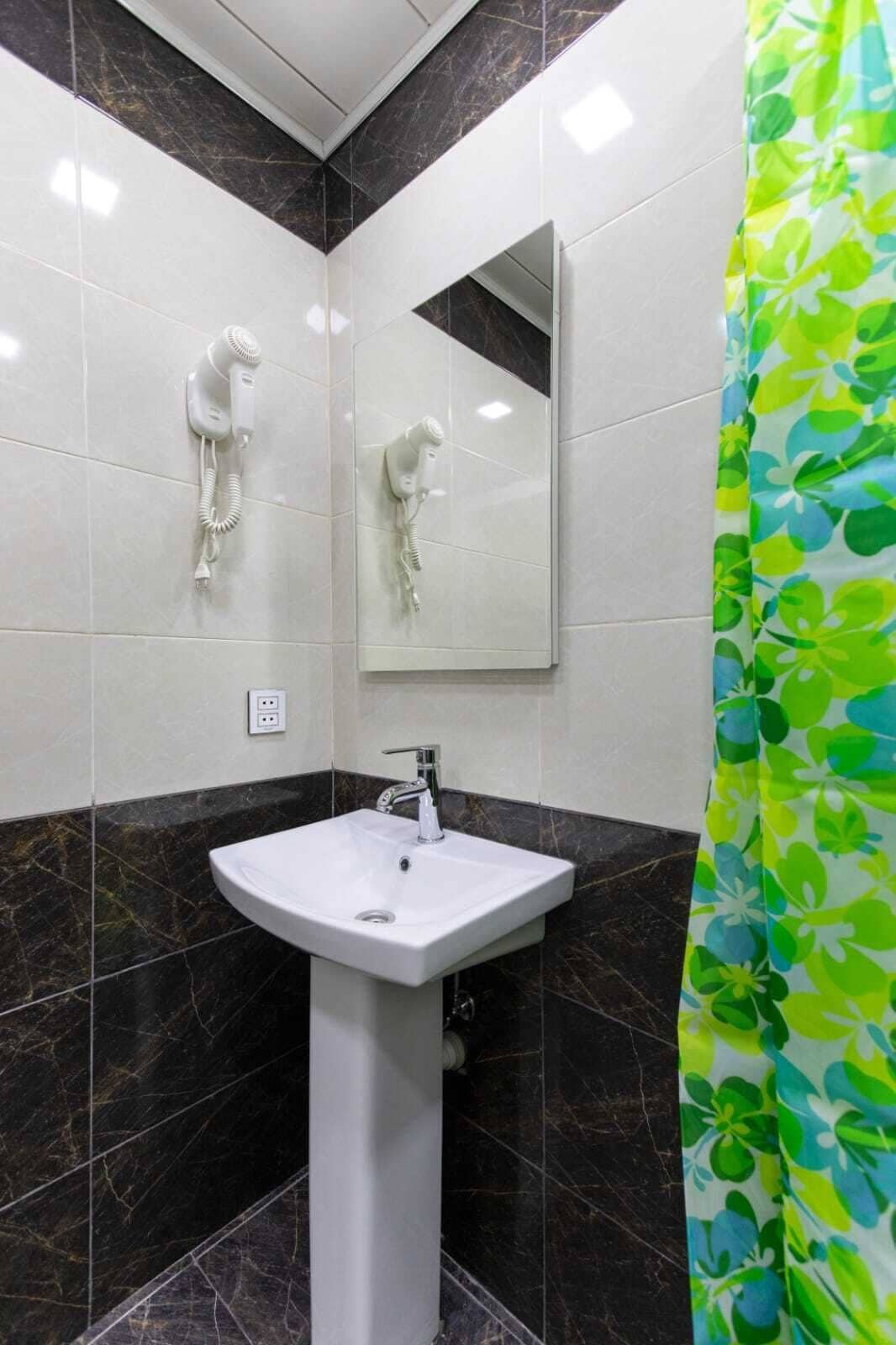 A bathroom with a white pedestal sink, a mirror, and two hair dryers mounted on the wall.