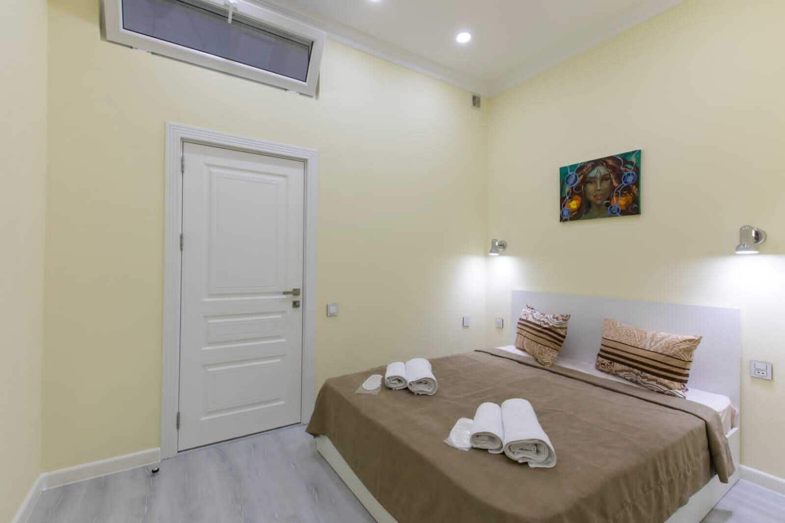 Un dormitorio con una cama, una puerta, un cuadro y una ventana.