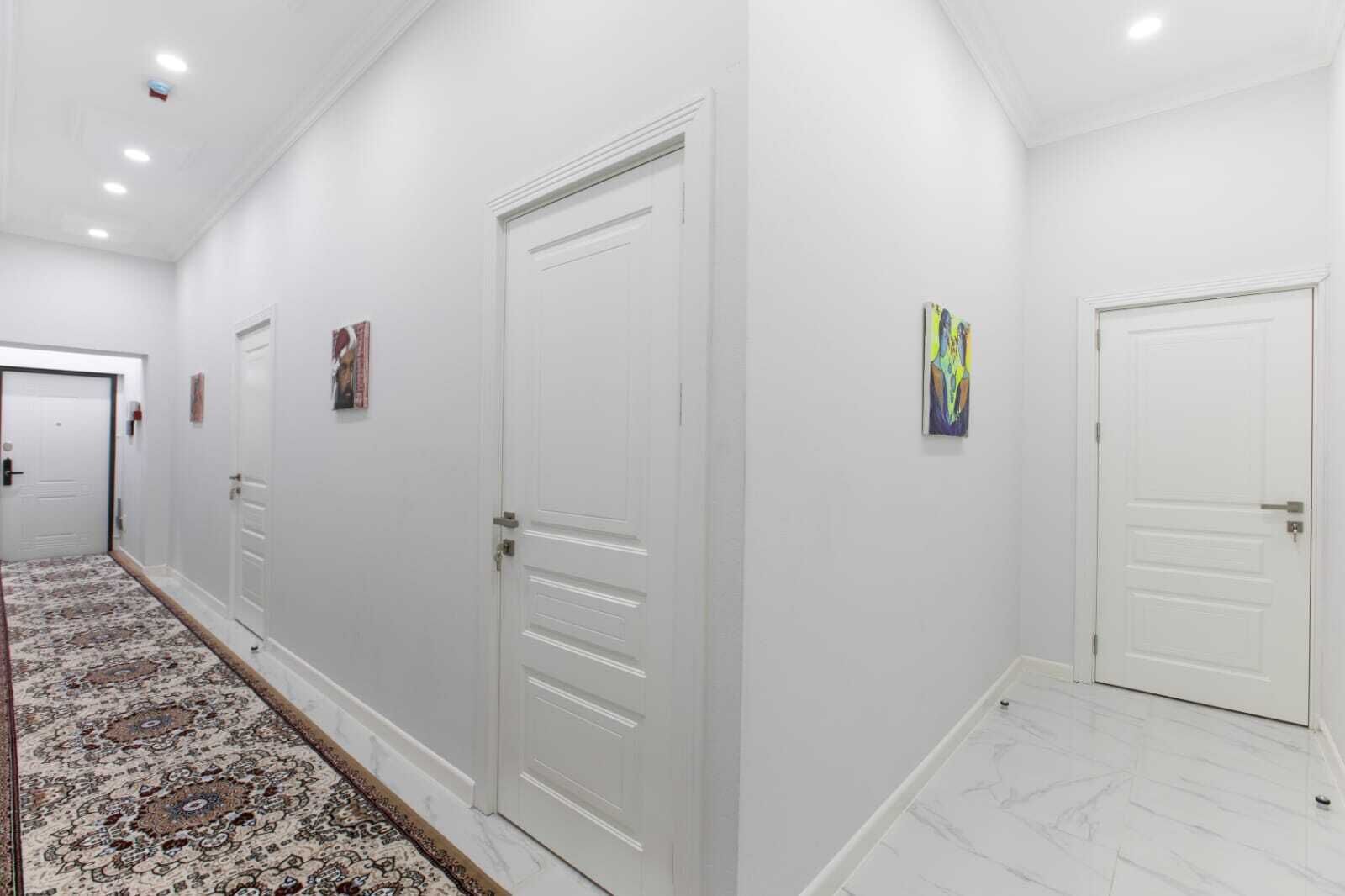 A hallway with white doors, a patterned carpet, and a tiled floor.
