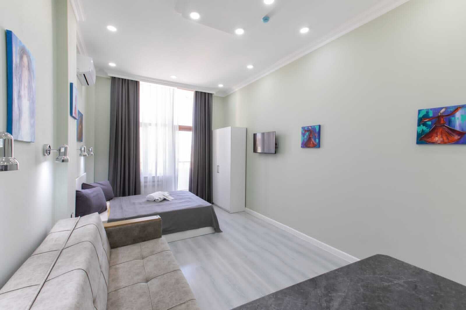 A modern hotel room with a bed, a seating area, a flat-screen TV, and artwork on the walls.